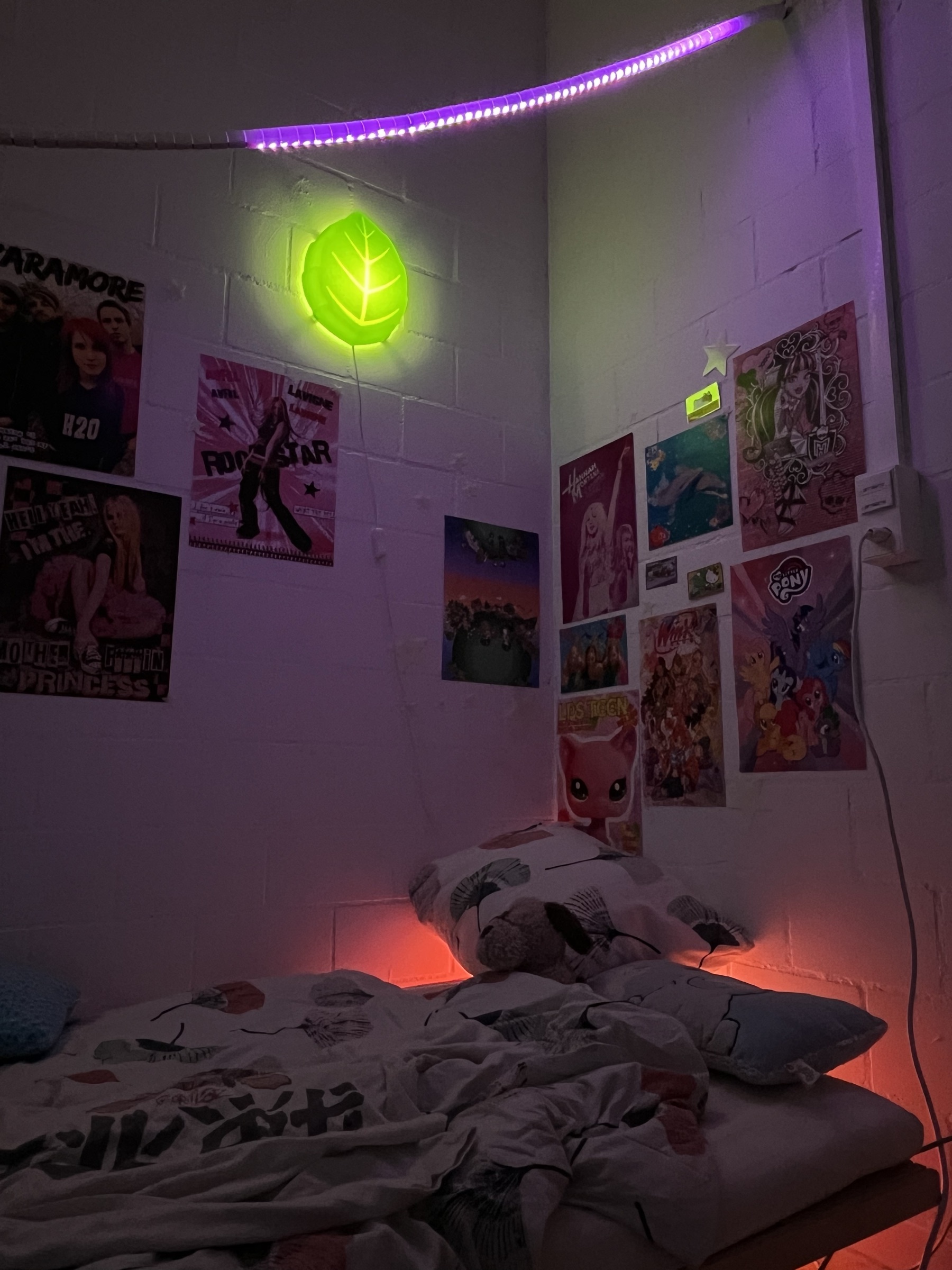The bed corner of the bedroom half, with the poster wall, the leaf wall lamp and the LED strip running along the ceiling.